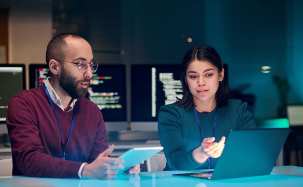 Two office workers around a computer and tablet